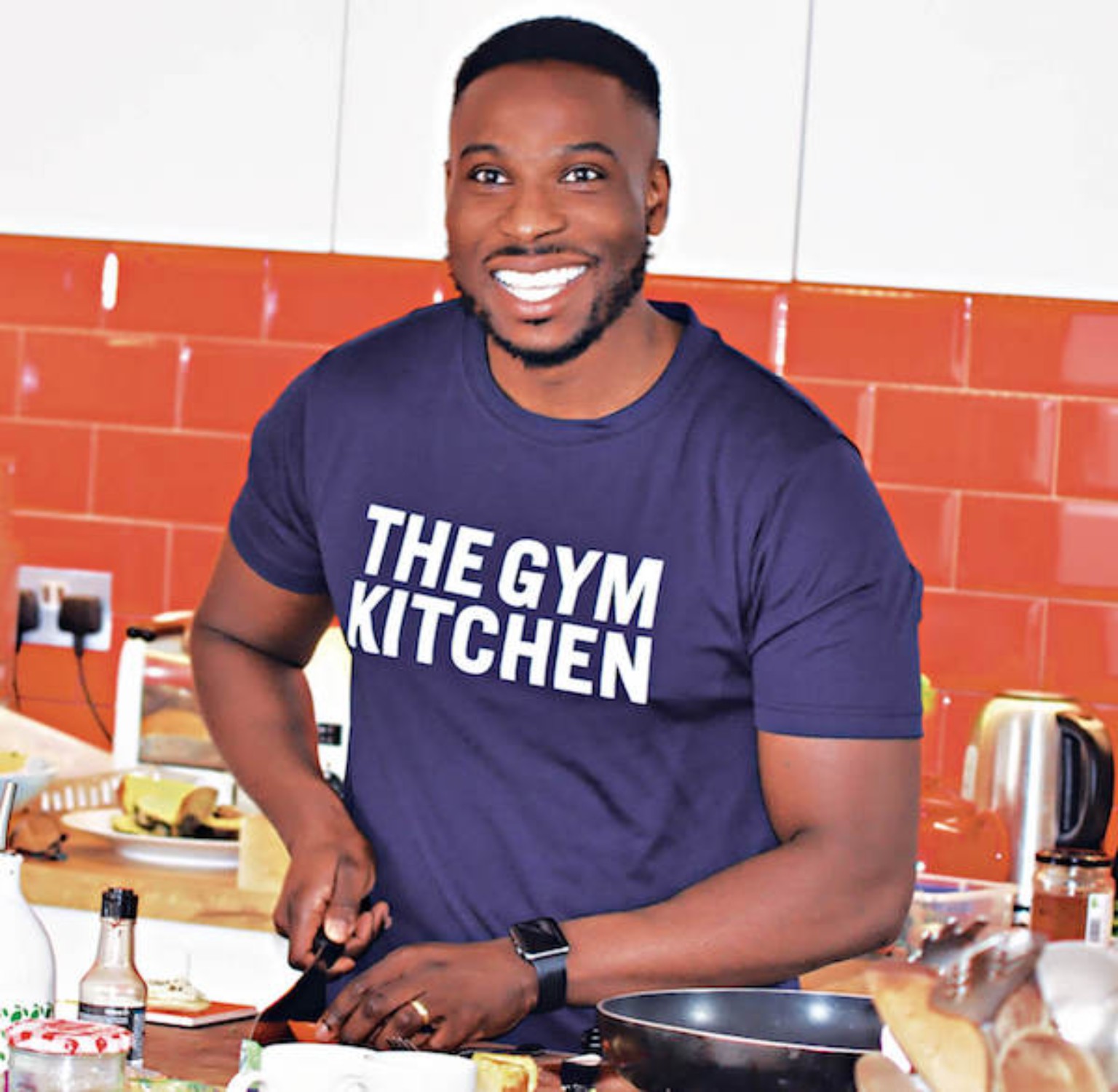 Segun Akinwoleola in a The Gym Kitchen shirt, preparing food